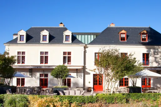 Exterior view of white building with red doors and windows, with small trees in front