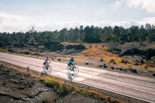 Two people riding a bike on an empty road with a forest in the background