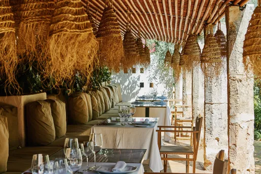 Outdoor patio with cushioned chairs and dining tables under a straw hut covering