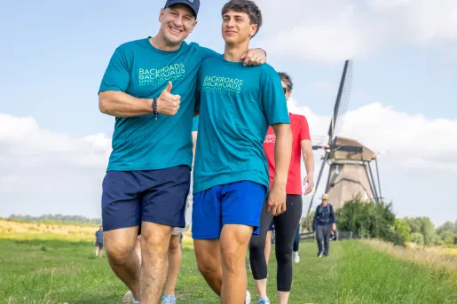 Two men with arms around their shoulders, smiling and giving a thumbs up