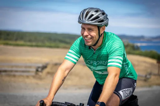 Man wearing green biking gear, smiling while biking on an empty road