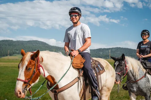 Man wearing sunglasses and a helmet, riding on the back of a horse