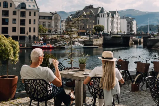 Man and woman sitting on a stone patio, drinking coffee and looking out to a river