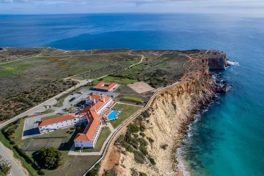 Sky view of white and red hotel building with a large cliff and ocean to the right