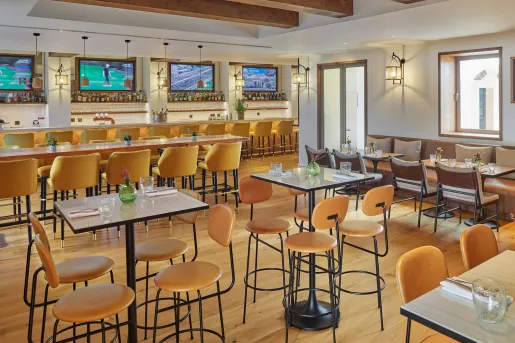 Bar and lounge with tall tables and chairs, with televisions on the wall