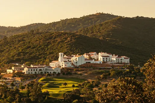 Wide, exterior view of white hotel building complex with tree-covered hills surrounding
