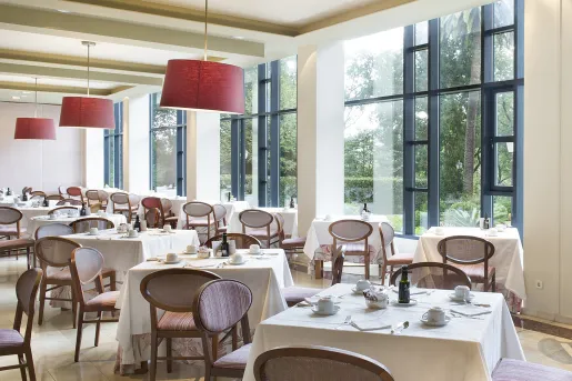 Dining hall with white, square tables and cushioned wooden chairs
