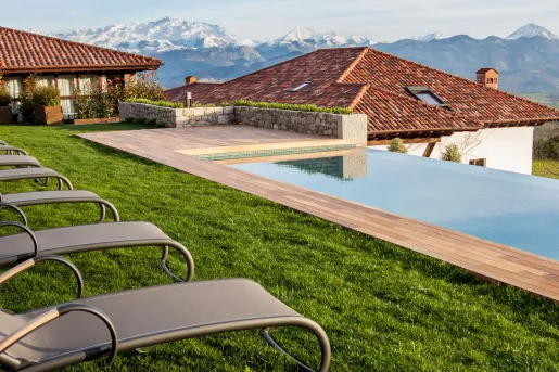 Outdoor pool surrounded by grass, gray reclining chairs and buildings in the background
