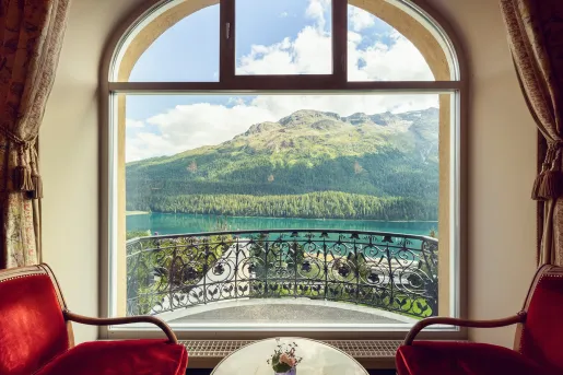 Two red velvet chairs with a large window looking out to a lake and mountains