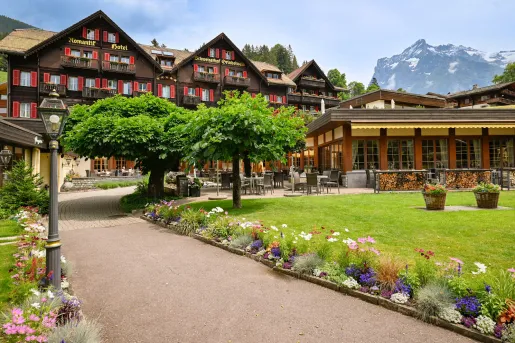 Exterior view of large brown and beige hotel building, with a grass area and small trees in front