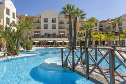 Beige hotel building with an outdoor pool in front, with large palm trees