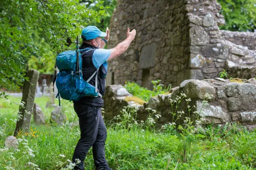 Man wearing a backpack, with both arms pointed out towards ruins