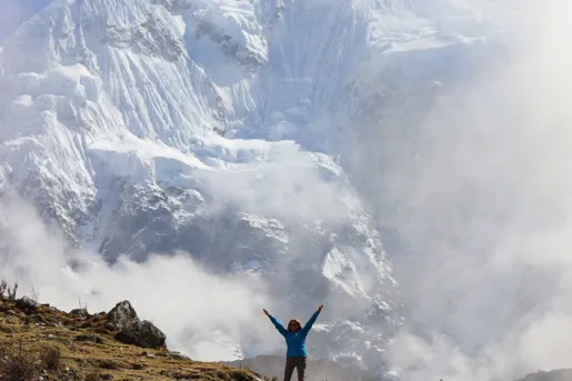 Person standing on top of a cliff with cloudy skies behind