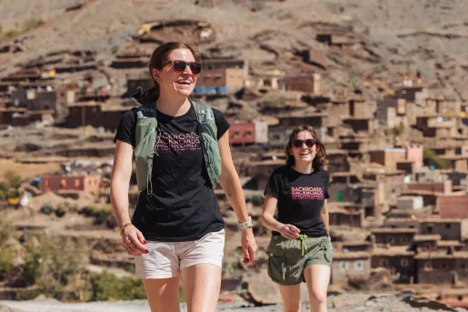 Two women smiling and walking with a town in the background