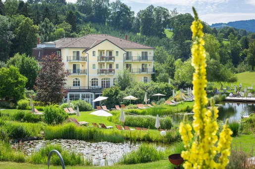 Exterior view of large, yellow hotel building with a large garden and fountain in front