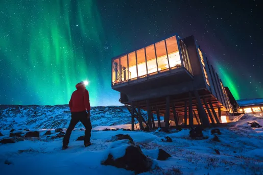 Man walking towards an elevated hotel building, with an aurora in the sky