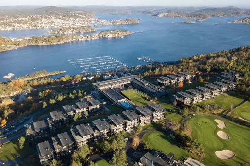 Sky view of buildings in a row, with a golf course in front and a lake in the back