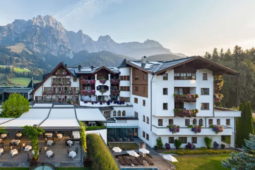 Exterior view of white and brown hotel building with large mountains in the background