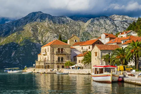 Shot of Croatian houses on coast, boats, mountain in distance.