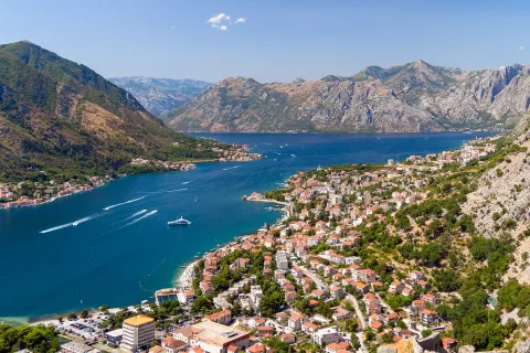 Bird's eye of Croatian riverside city, mountains all around, boats in river.