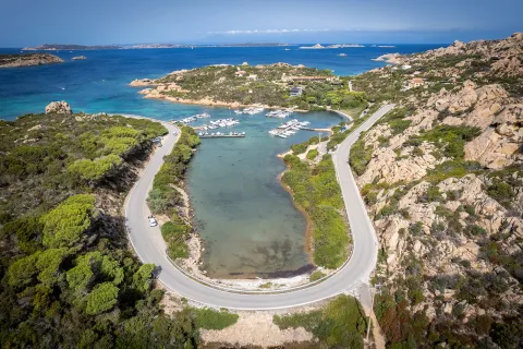 Bird's eye shot of a "U" shaped road on the Italian coastline, small boats and piers in distance.