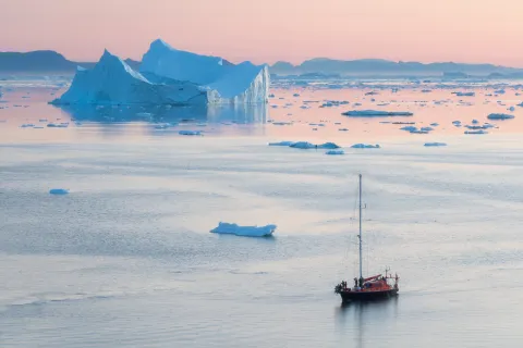 a ship floating on reflective water during a pink sunset