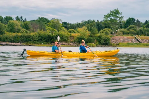 Two men inside of a yellow kayak, paddling in an open lake