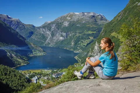 Woman sitting on a boulder, looking out to large mountains and a lake