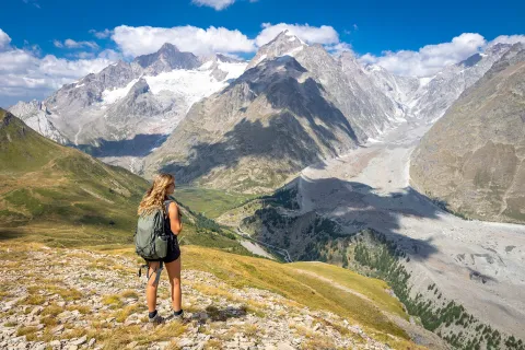 Woman wearing a backpack, looking out to a large valley of mountains and trees