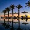 Sunset shot of still resort pool, palms, recliners.