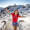 Guest emoting to camera, white walled coastal buildings behind her.
