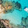 Overhead shot of guests on the beach, some are on small boats in the water.