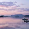 Two sailboats on a still lake during purple sunset.