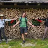 Three guests in front of wooden building, one in center, the other two gesturing to them.