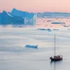 a ship floating on reflective water during a pink sunset
