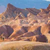 Two people standing on top of a large, orange canyon looking at larger canyons