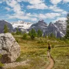 Woman walking along a dirt trail with large mountains in the distance