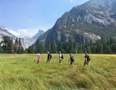 Guests hiking through grassy field, mountains in background.