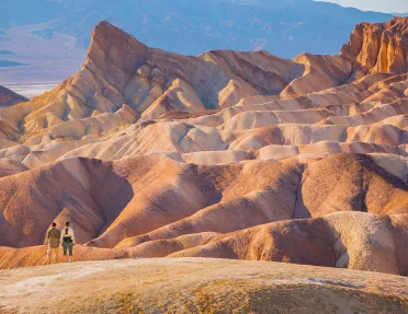 Two people standing on top of a large, orange canyon looking at larger canyons
