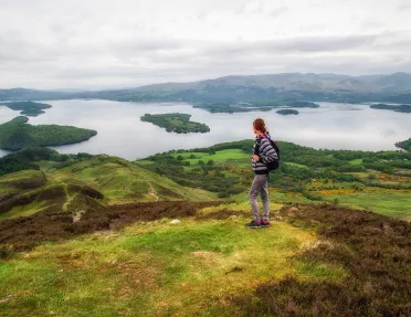 Woman standing on top of a grassy hill, looking out to smaller hills