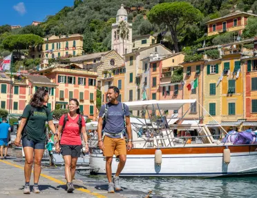 Two women and one man walking along a boat dock, with orange buildings in the background