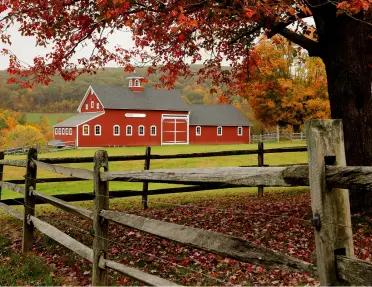 Red barn with a large field and wooden fence in front