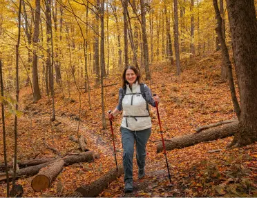 Woman smiling while hiking in a forest, with orange leaves and trees
